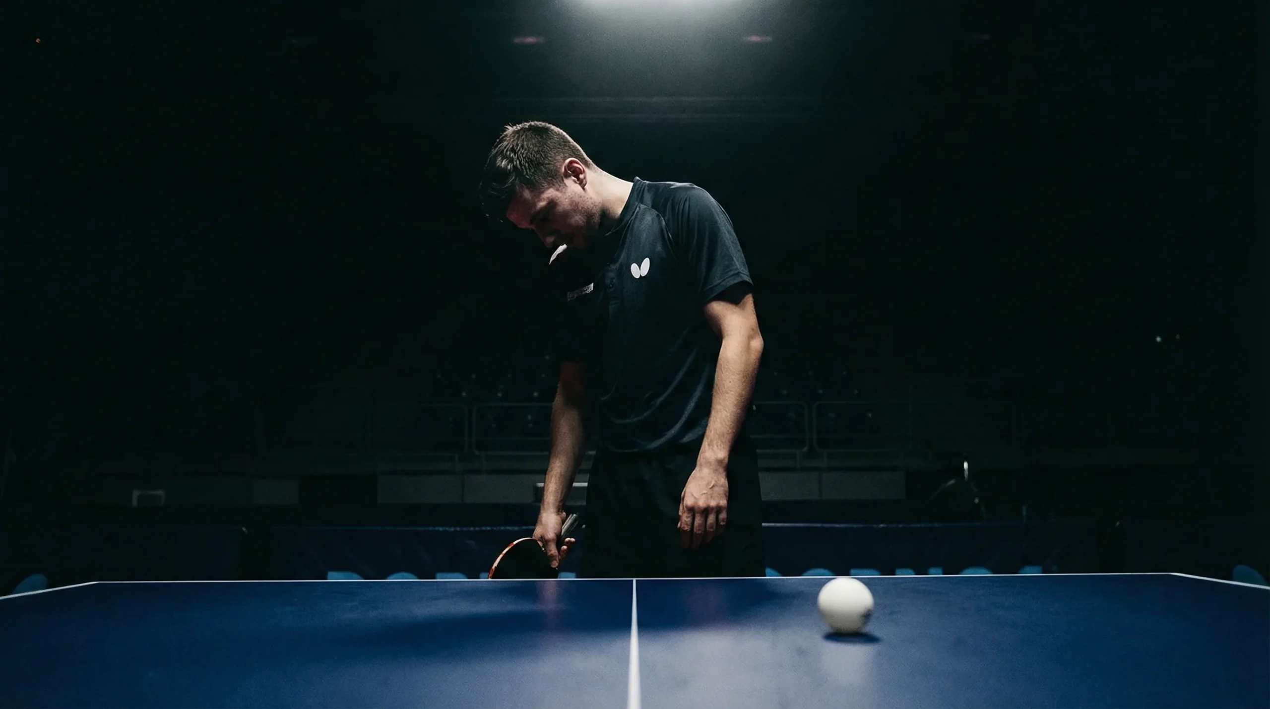 Joueur de tennis de table frustré après un point perdu, raquette baissée sous un éclairage dramatique