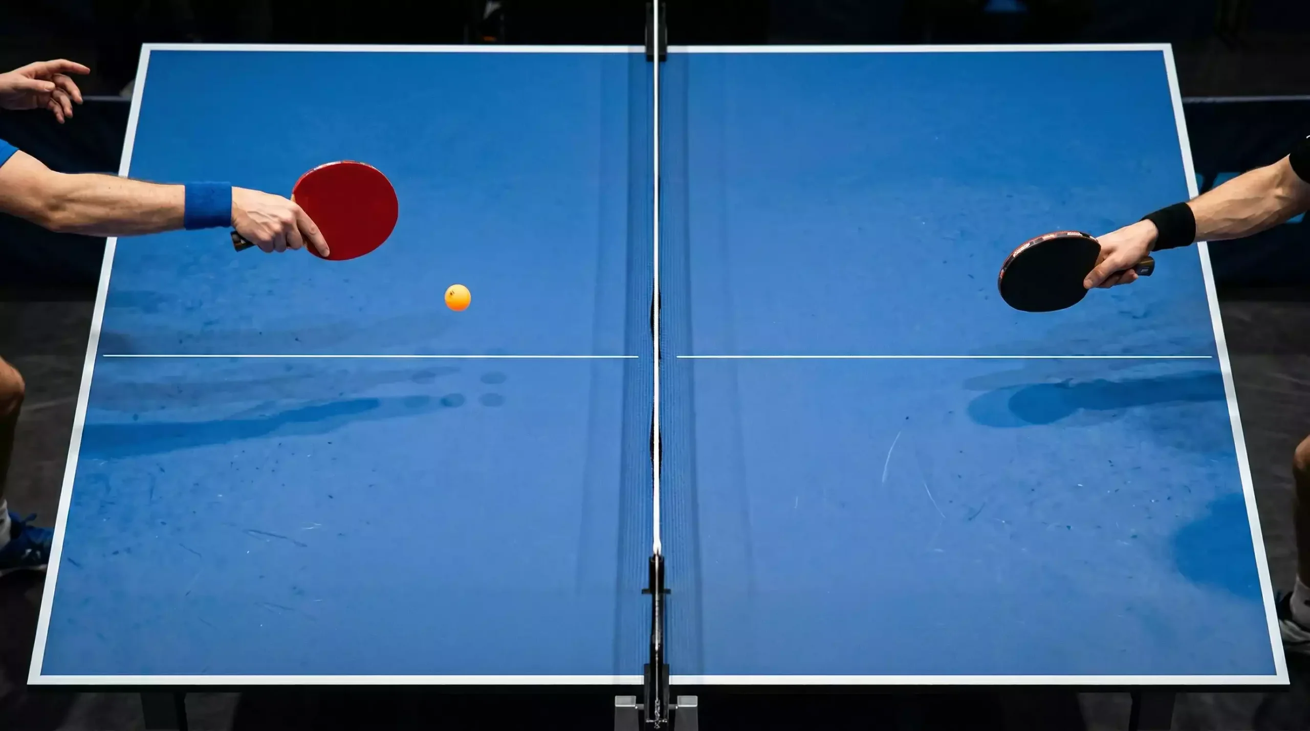 Vue plongeante sur une table de tennis de table pendant un échange avec la balle en mouvement entre deux raquettes